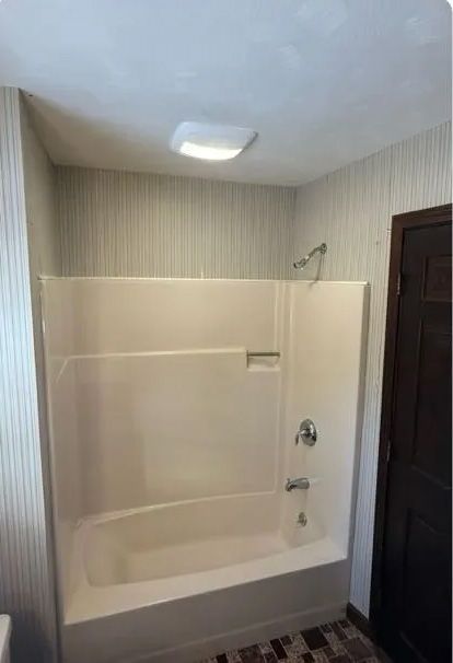 Bathroom with white tub and shower enclosure, light fixture, and patterned wallpaper.