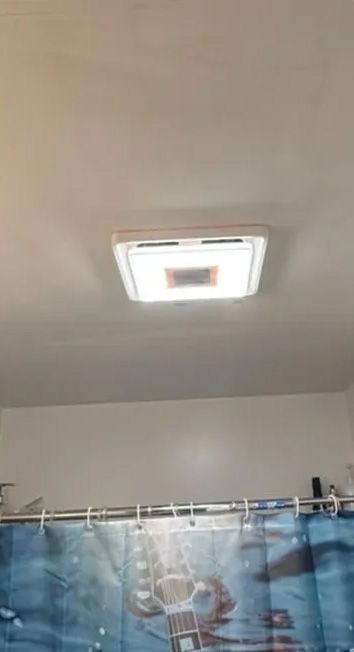 Bathroom ceiling light fixture centered above a shower curtain rod. White ceiling, white fixture, blue shower curtain.