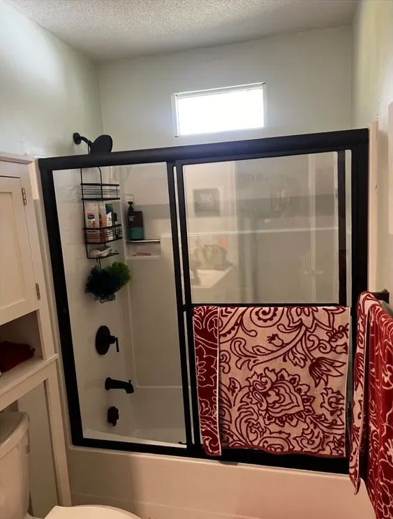 Bathroom with black framed shower door, red towels, and a small window above the shower.