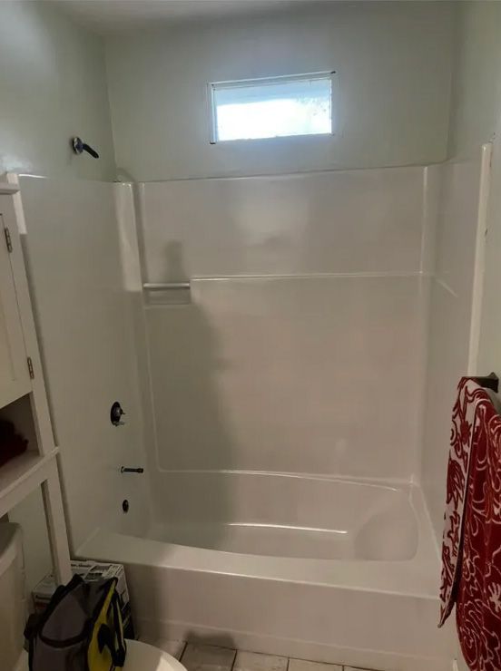 White bathtub-shower combo in a bathroom. Features a small window, faucet, and a towel rack.