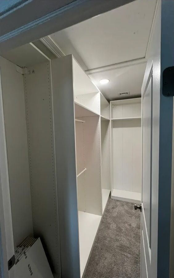 White walk-in closet with shelves and hanging rods; gray carpet, white door.