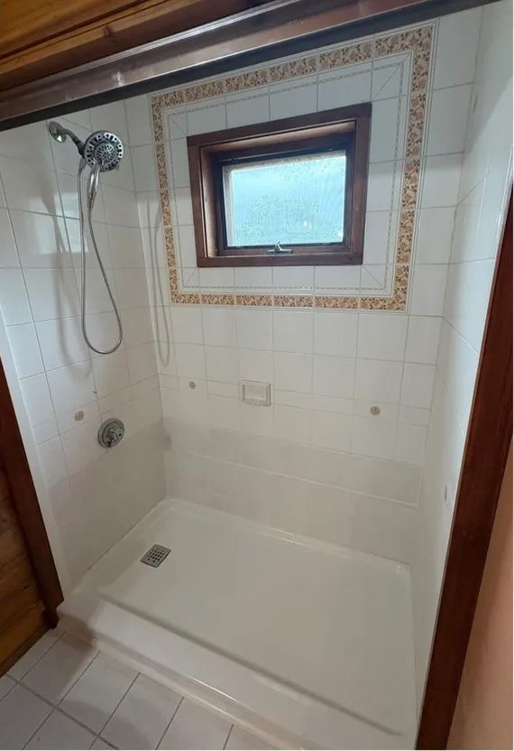Shower stall with white tiles, small window, and showerhead.