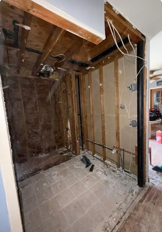 Bathroom renovation in progress, walls open to studs, plumbing and wiring exposed.