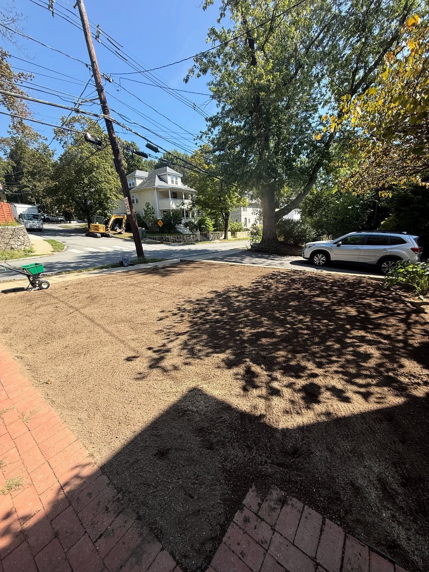 Cleared dirt patch in front yard, brick steps, street view with trees, parked SUV, and utility pole.