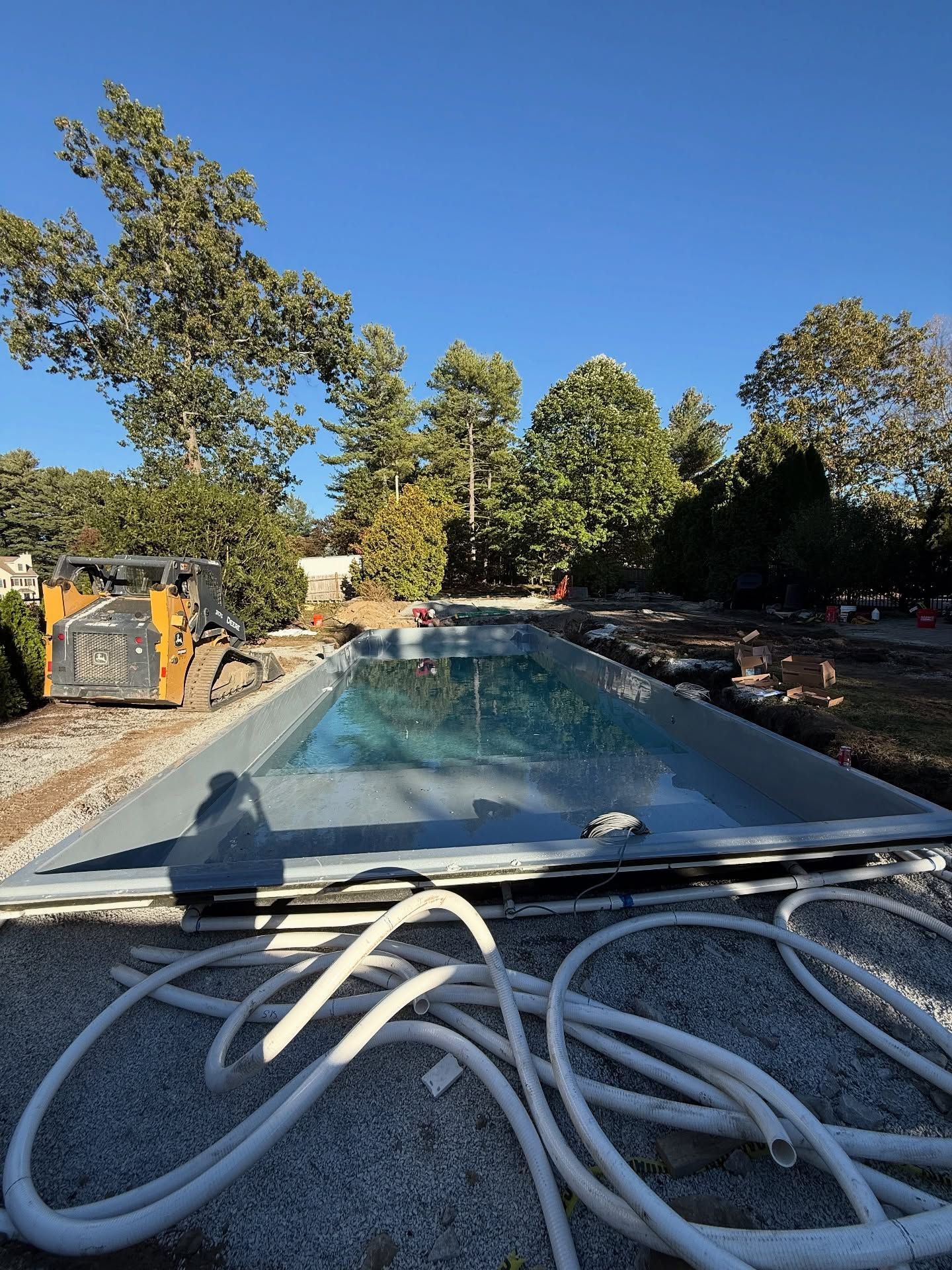 Pool construction site with a partially filled pool, clear sky, and a skid steer.