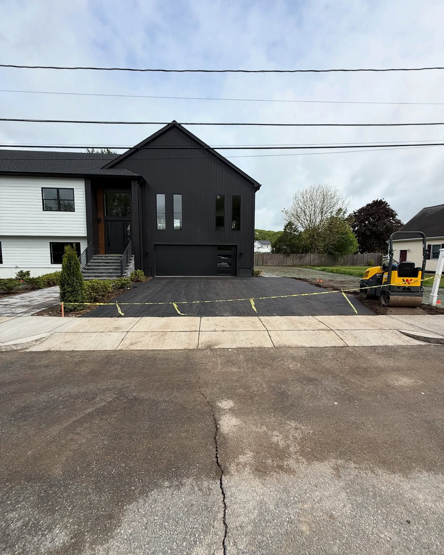 Black and white house with new asphalt driveway. A small compactor is visible.