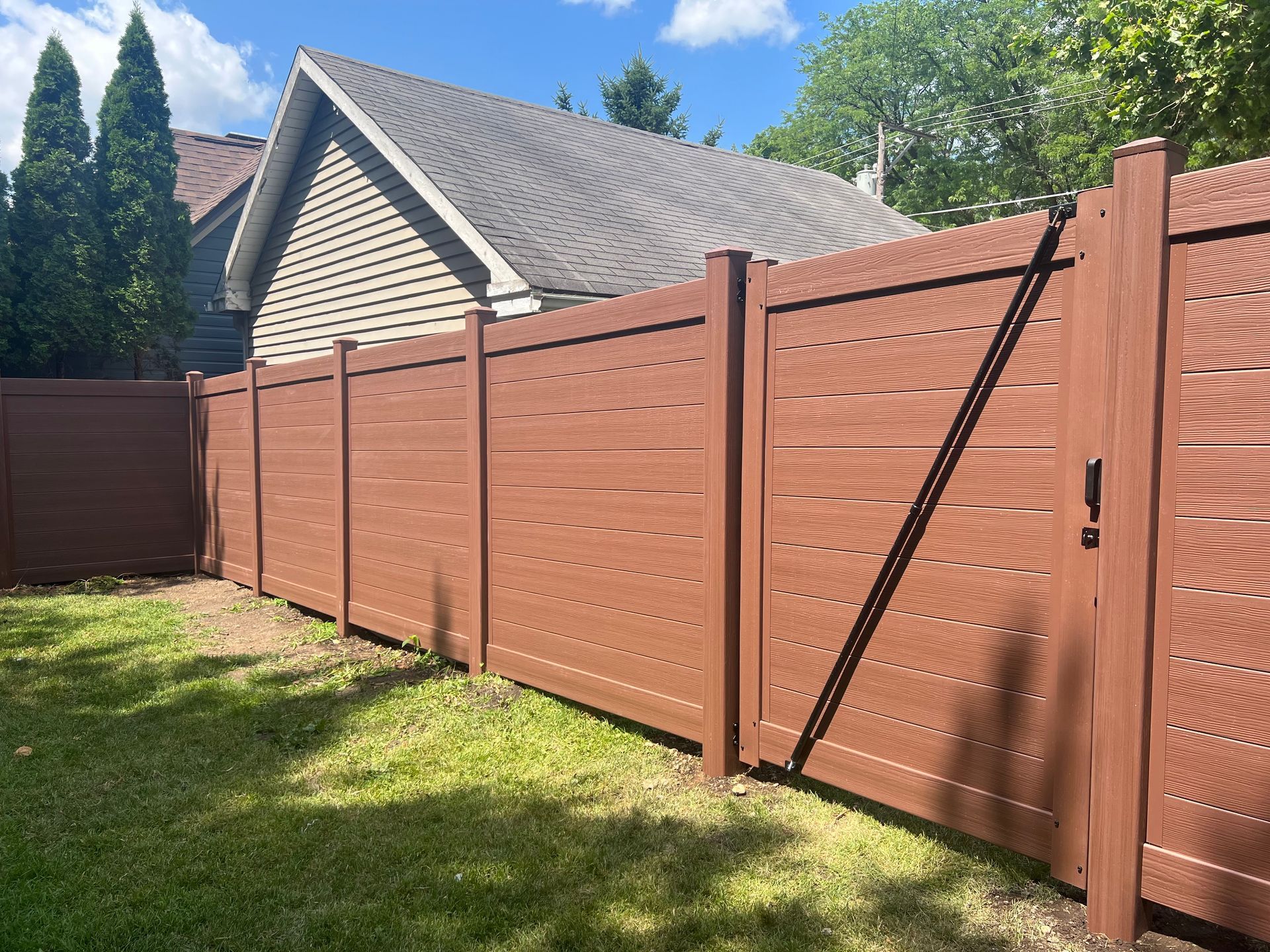A brown wooden fence surrounds a lush green yard in front of a house.