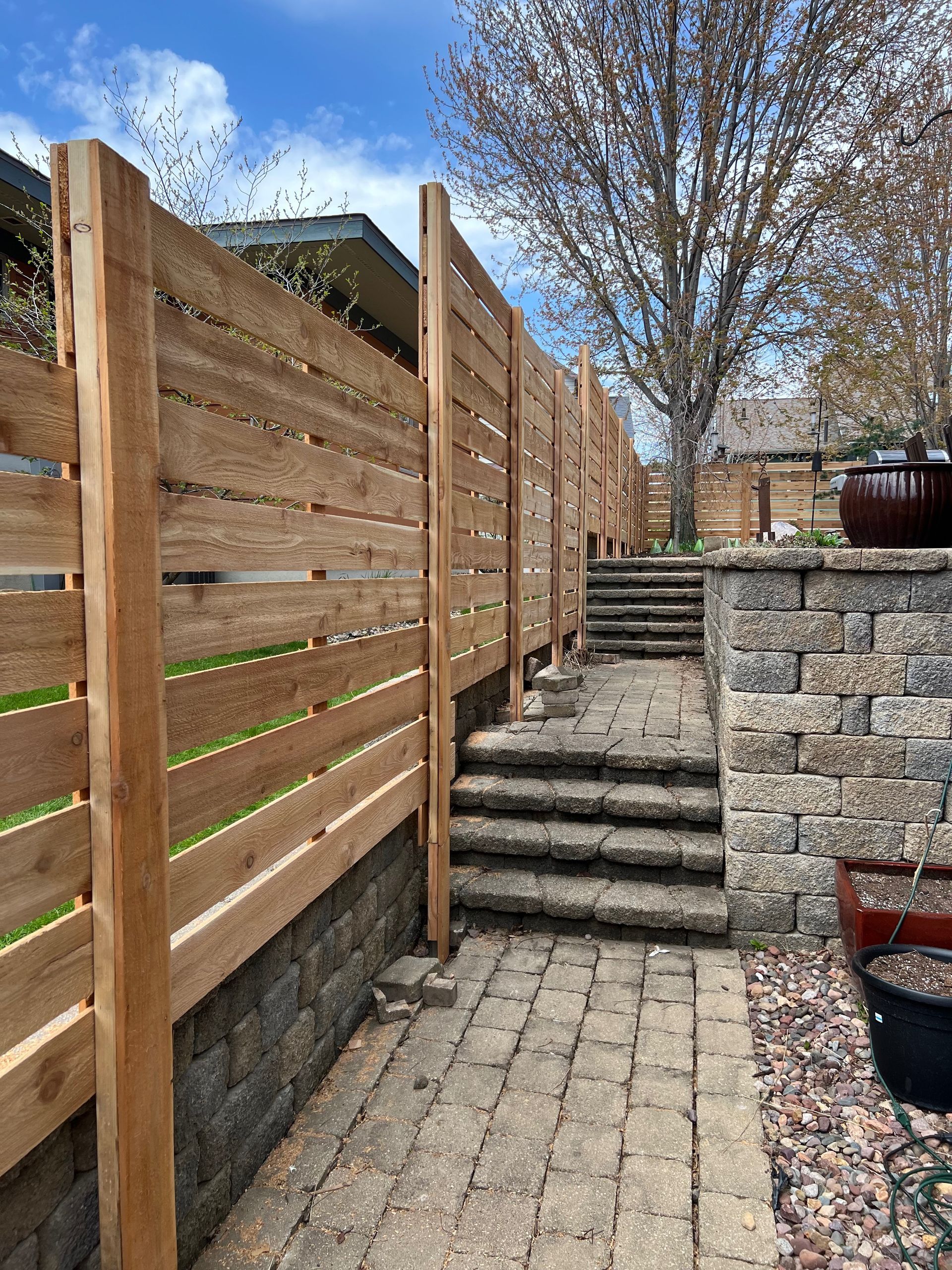 A wooden fence surrounds a brick walkway with stairs leading to a house.