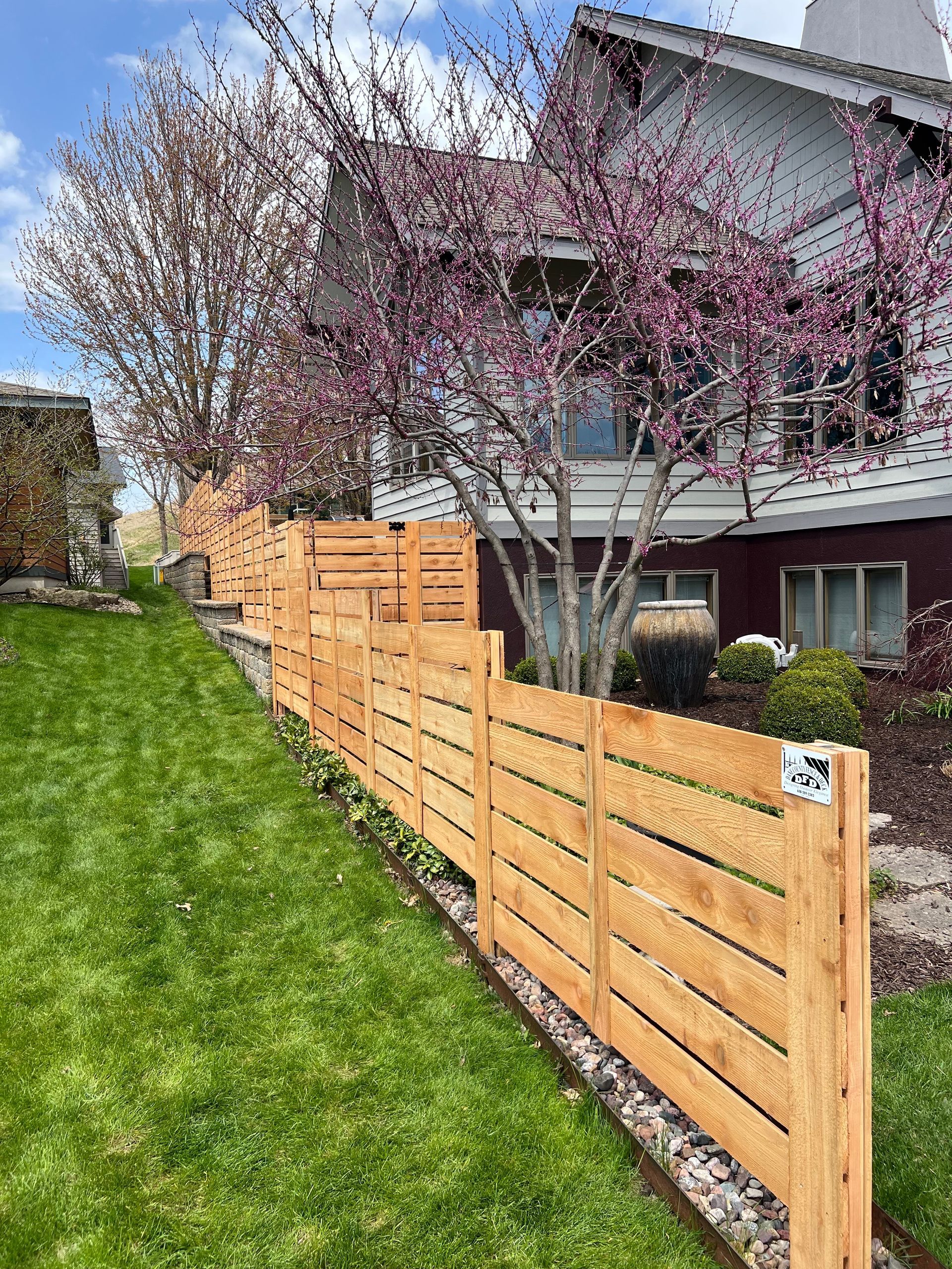 A wooden fence surrounds a lush green lawn in front of a house.