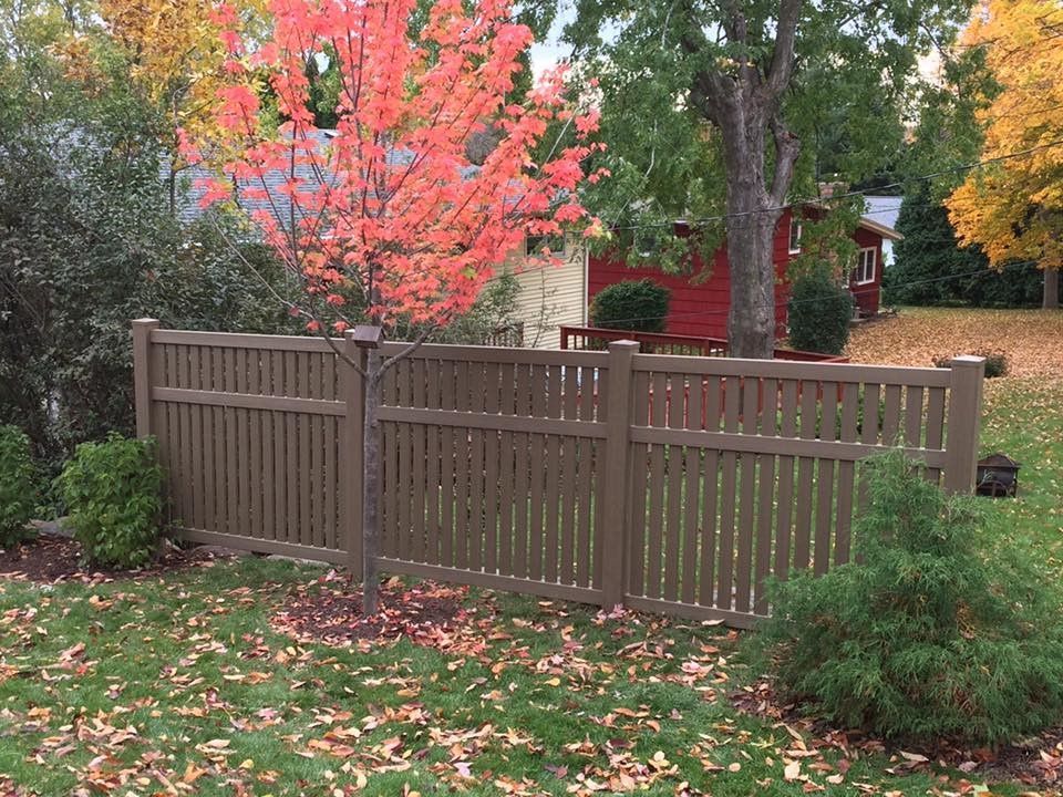 A wooden fence surrounds a lush green yard with a red house in the background.