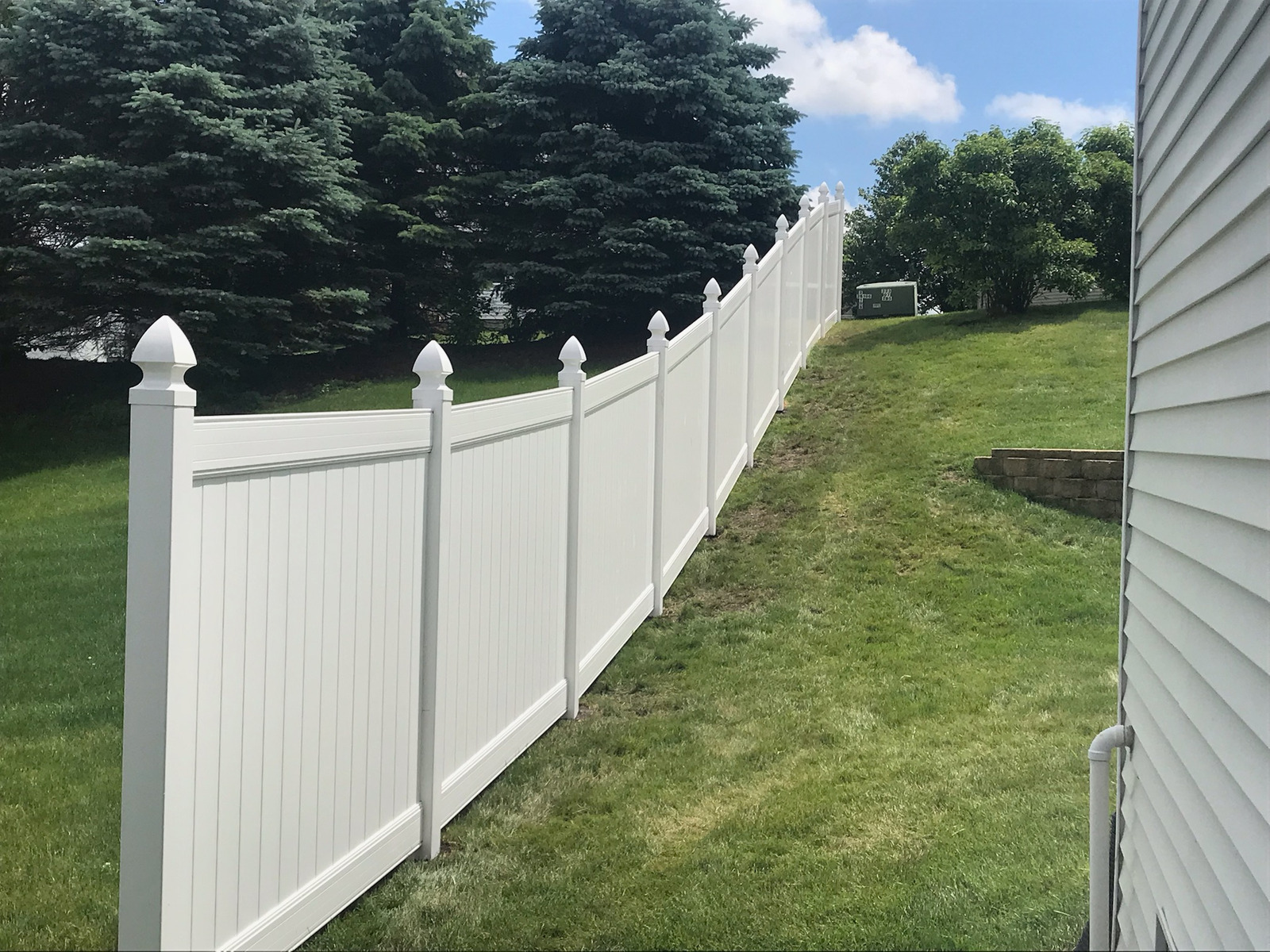 A white fence surrounds a lush green yard next to a house.