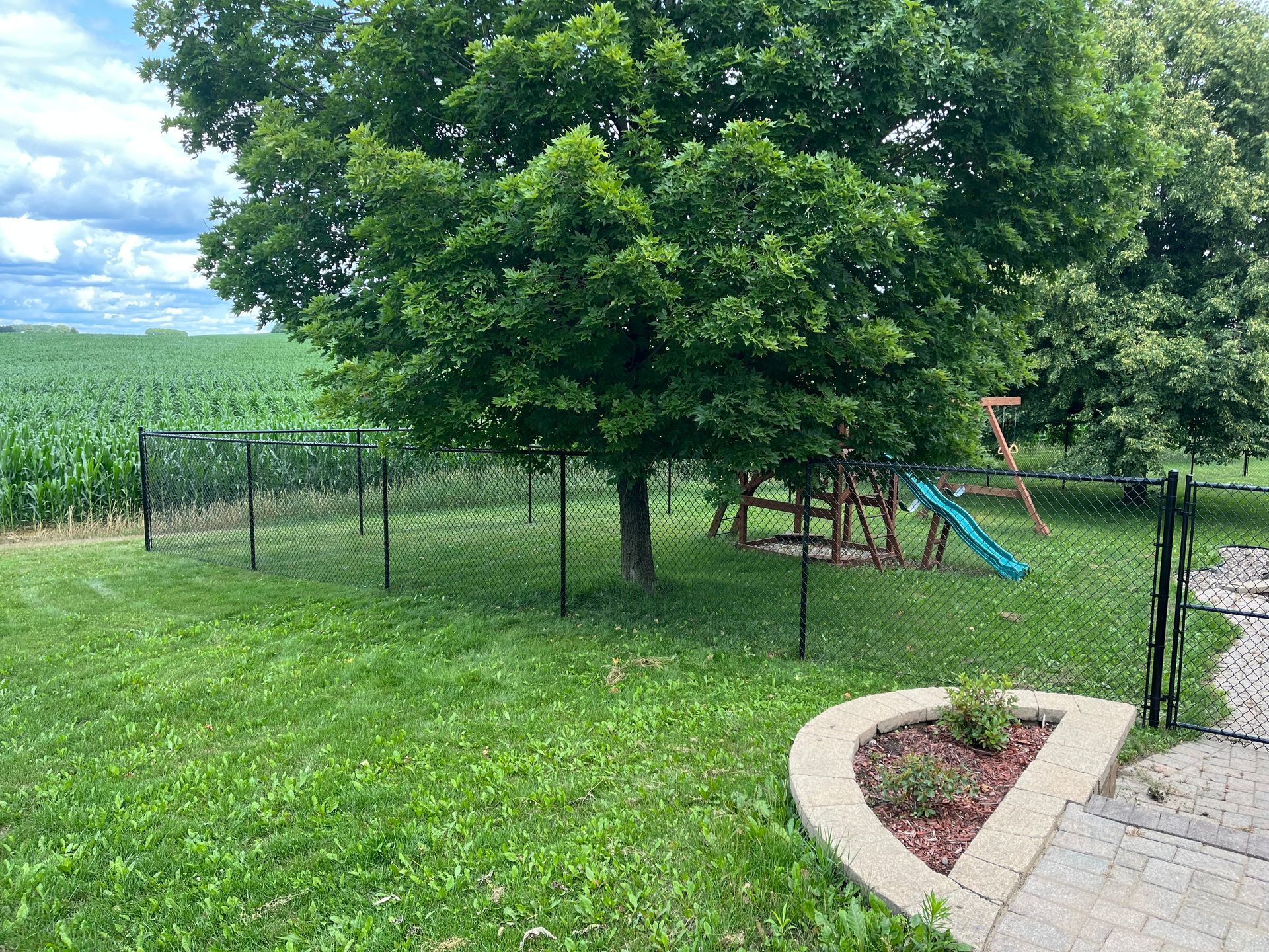 A backyard with a swing set and a tree in the middle of it.