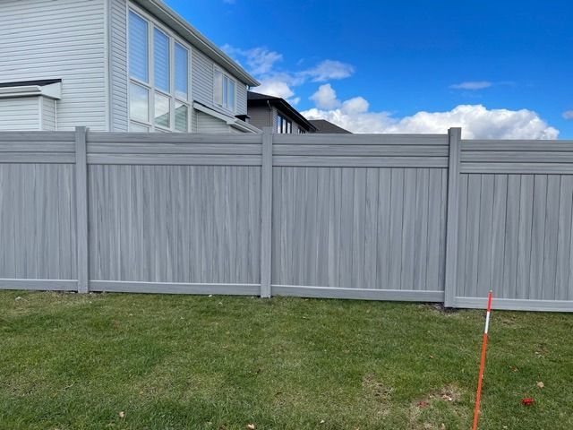 A gray fence is in the backyard of a house.