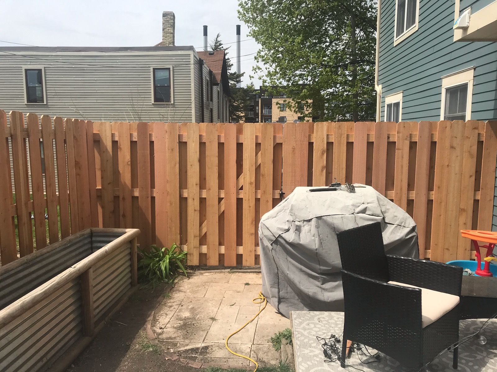 A wooden fence surrounds a patio area with a grill and chairs.