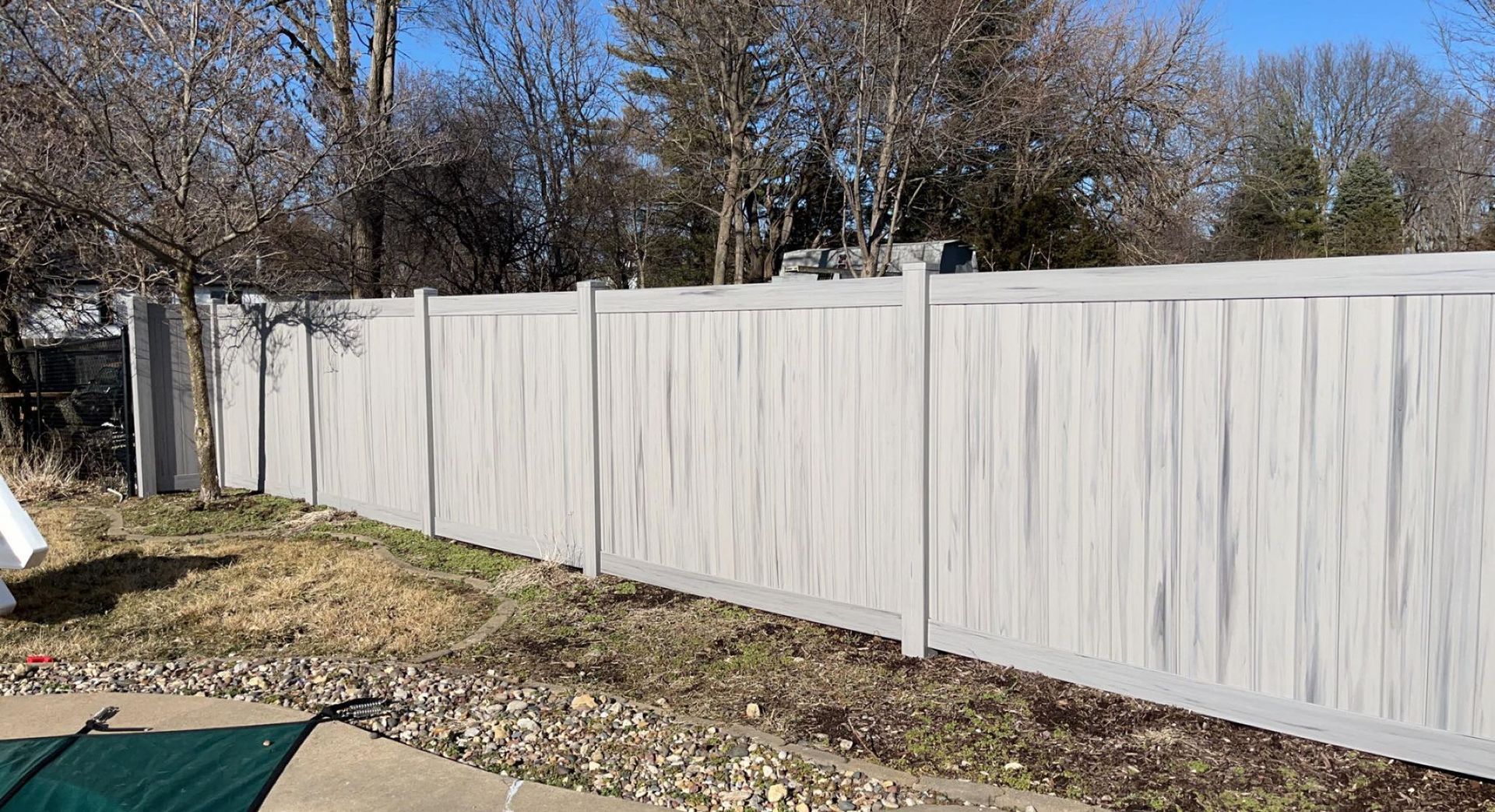 A white vinyl fence surrounds a swimming pool in a backyard.
