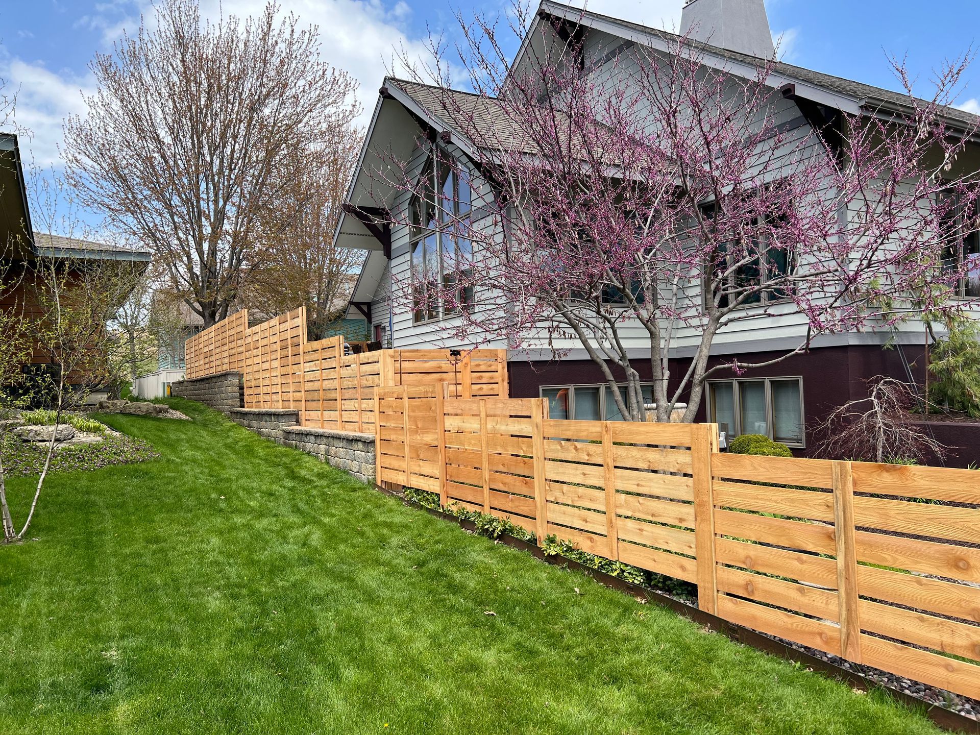 A wooden fence surrounds a lush green yard in front of a house.