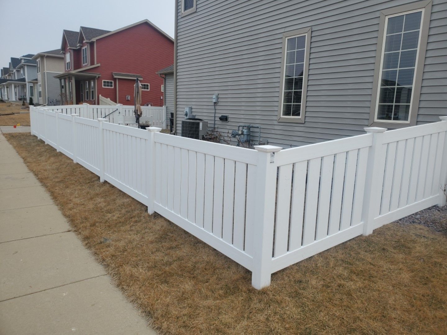 A white fence is surrounding a house in a residential area.