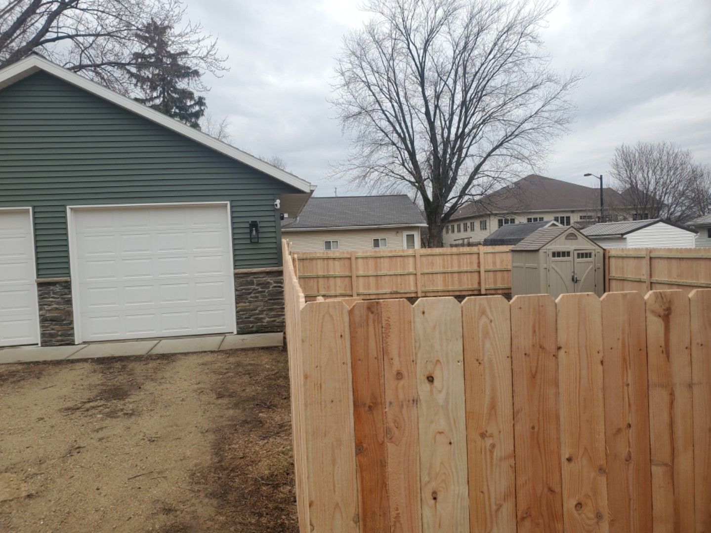 A wooden fence is in front of a garage and a house.