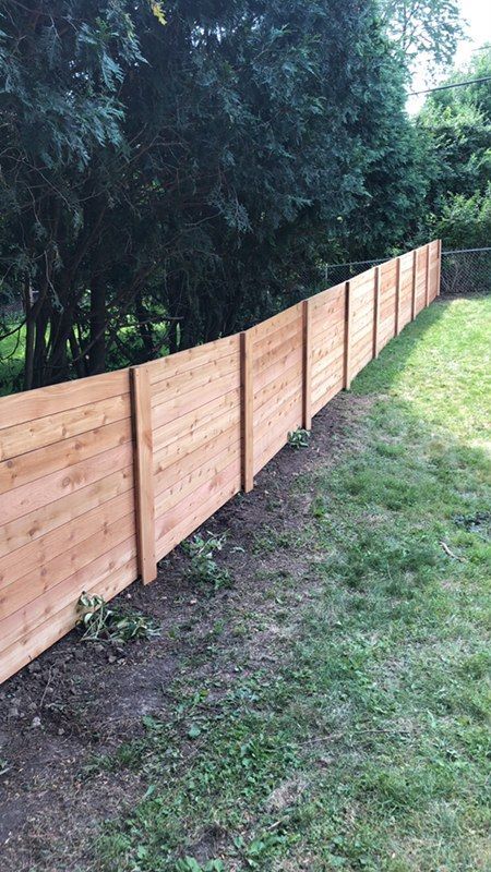 A wooden fence is surrounded by trees in a backyard.