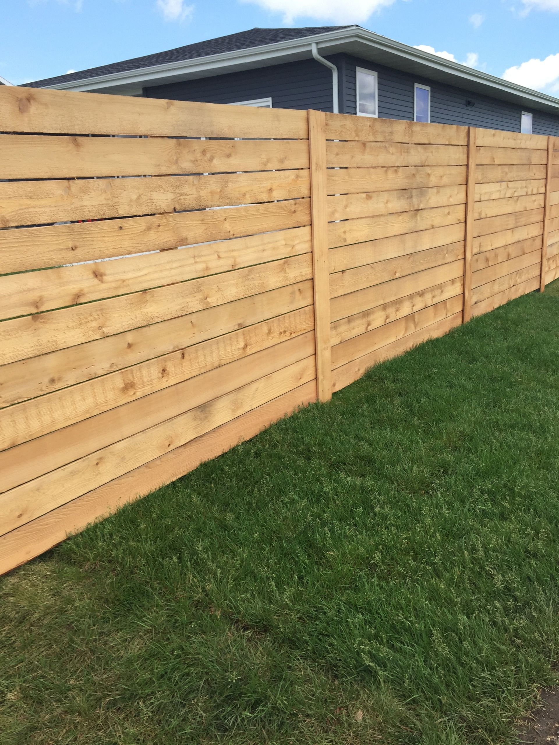 A wooden fence surrounds a lush green lawn in front of a house.