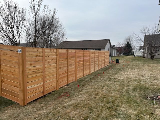 A wooden fence is sitting in the middle of a grassy field next to a house.