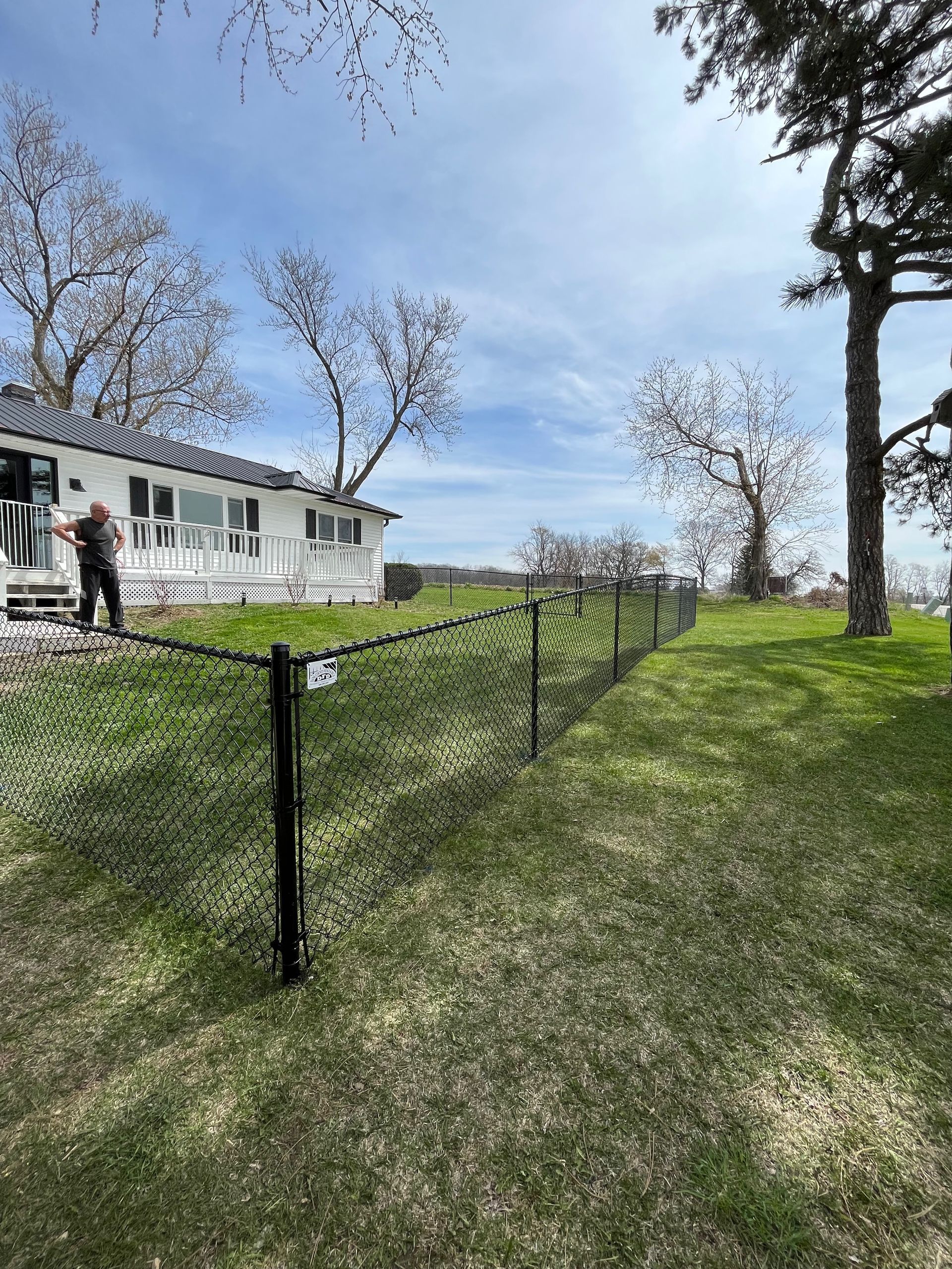 A man is standing in front of a house with a chain link fence.