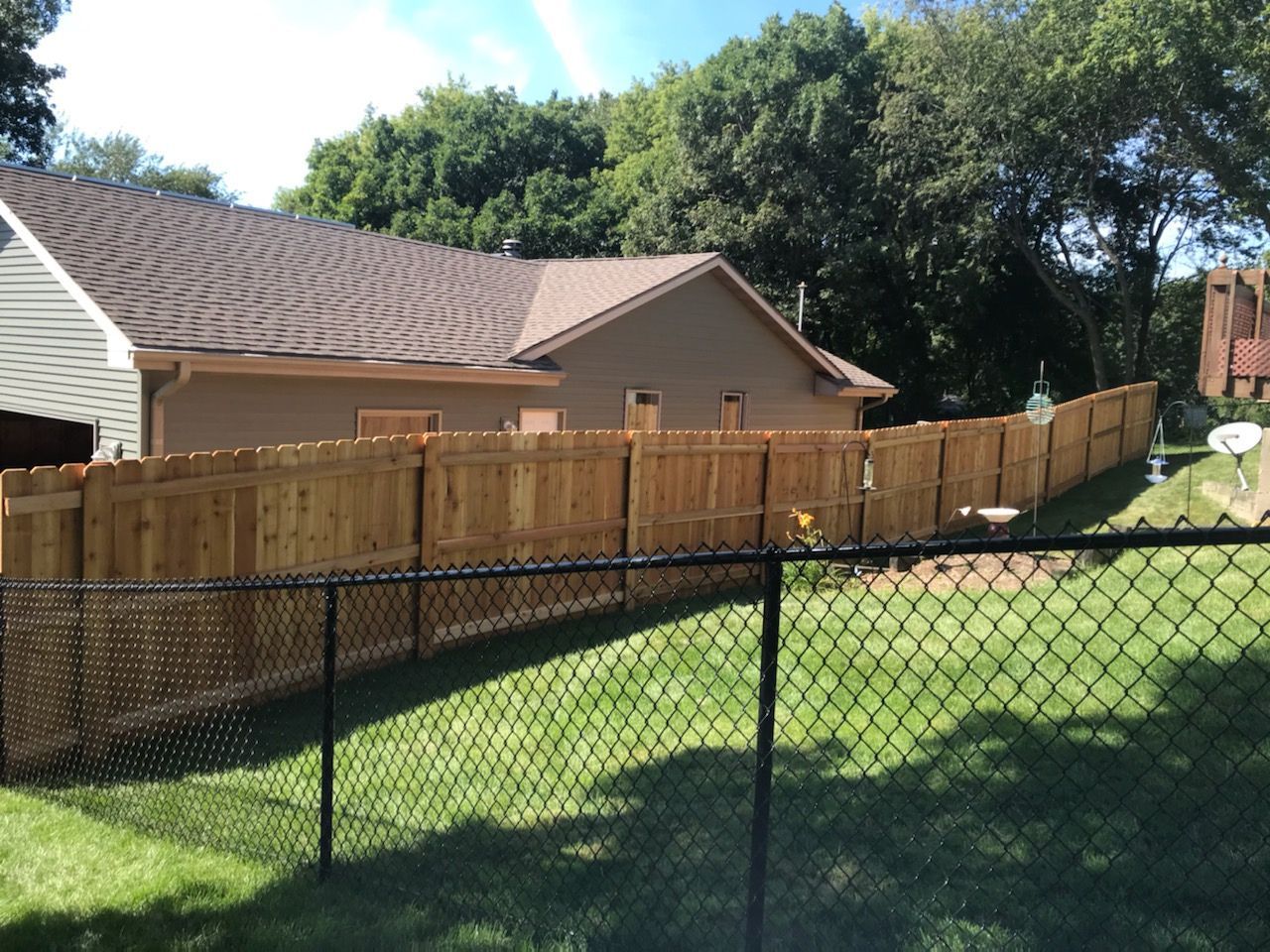 A wooden fence surrounds a backyard with a chain link fence.