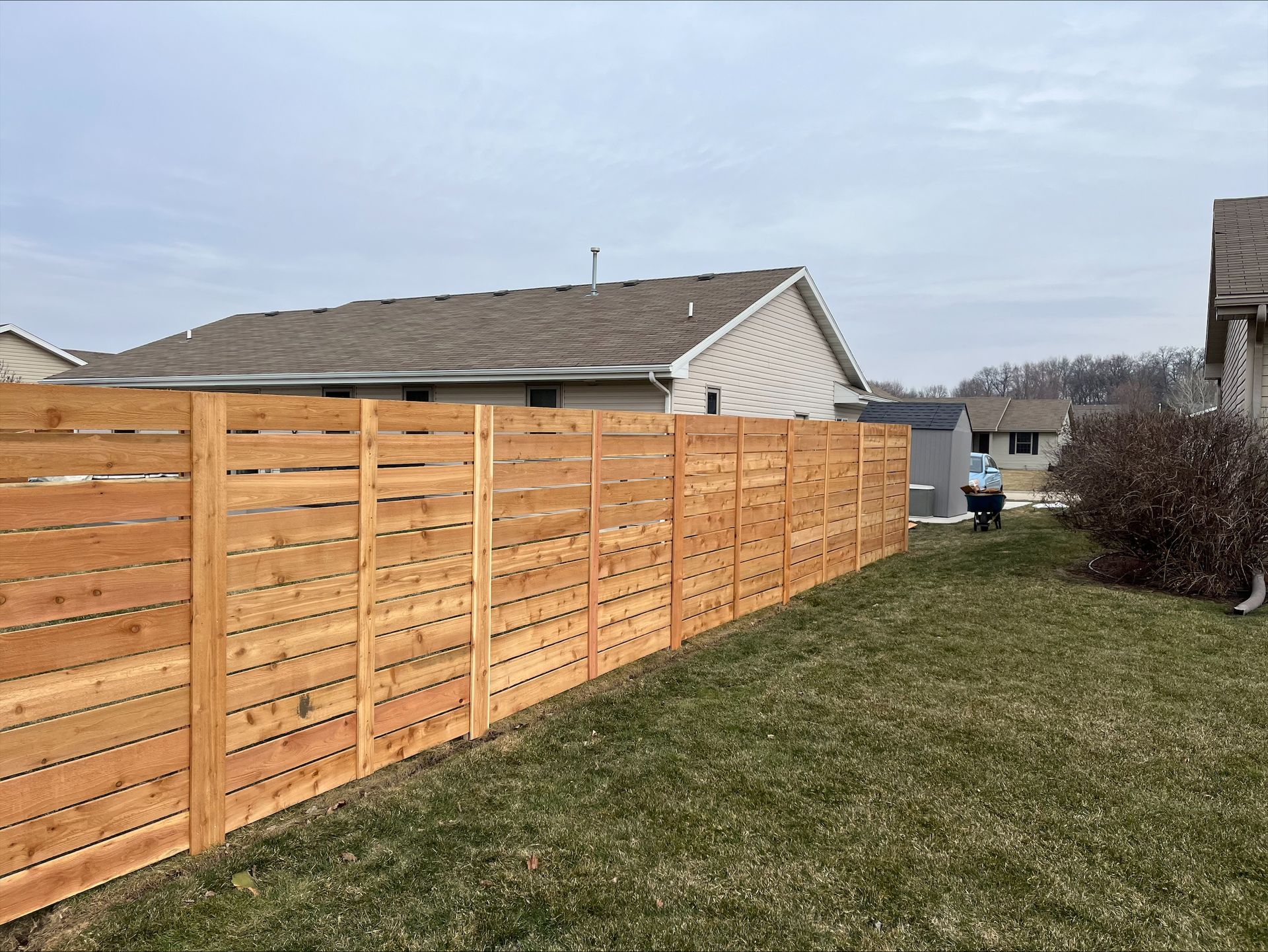 A wooden fence surrounds a lush green yard in front of a house.