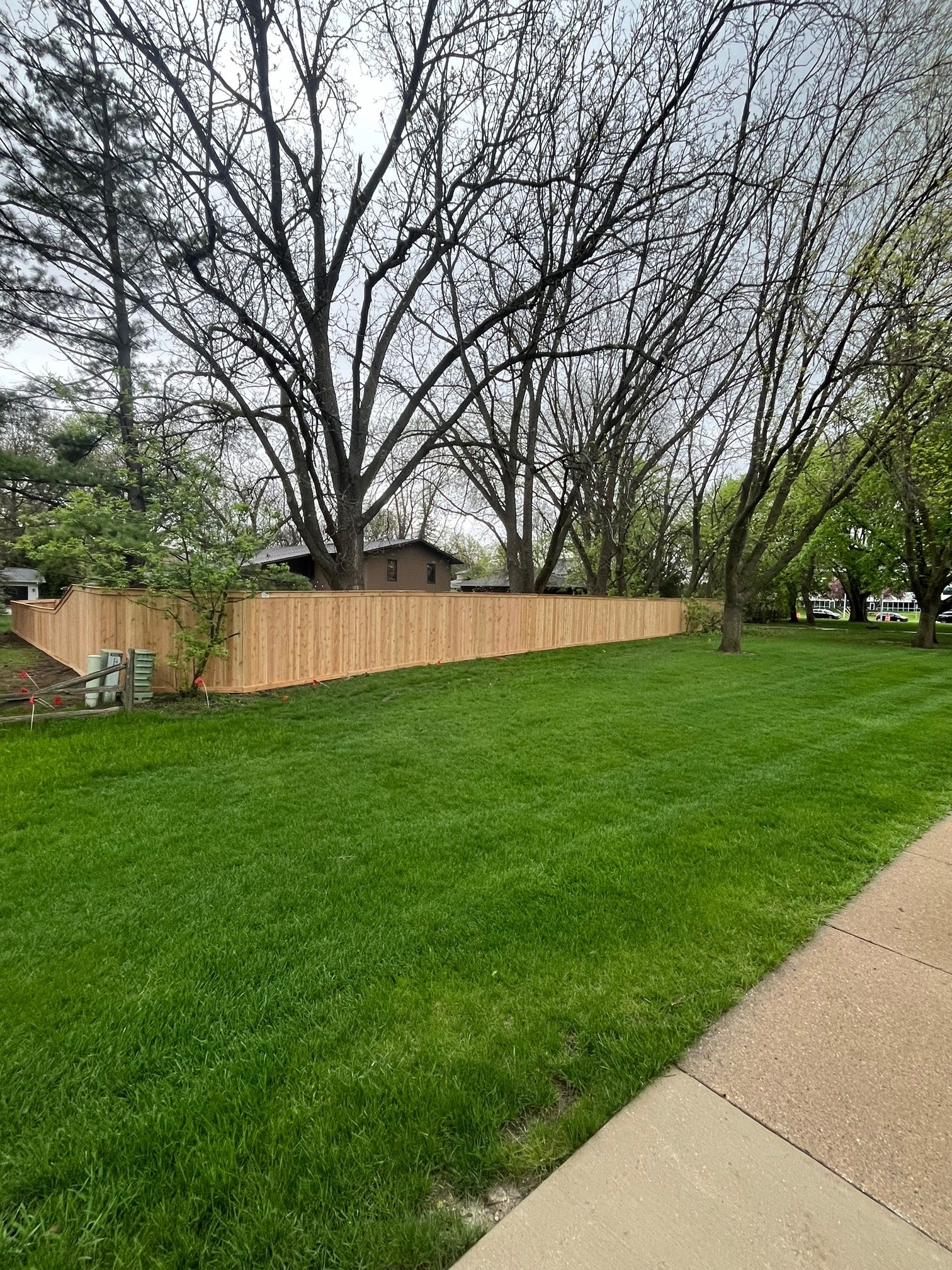 A wooden fence surrounds a lush green lawn next to a sidewalk.