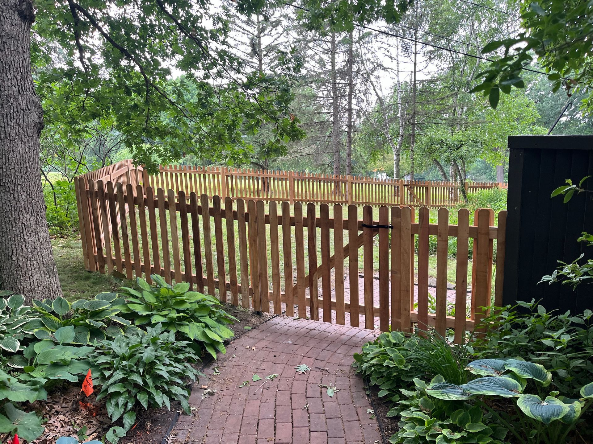 A wooden picket fence surrounds a brick walkway in a garden.