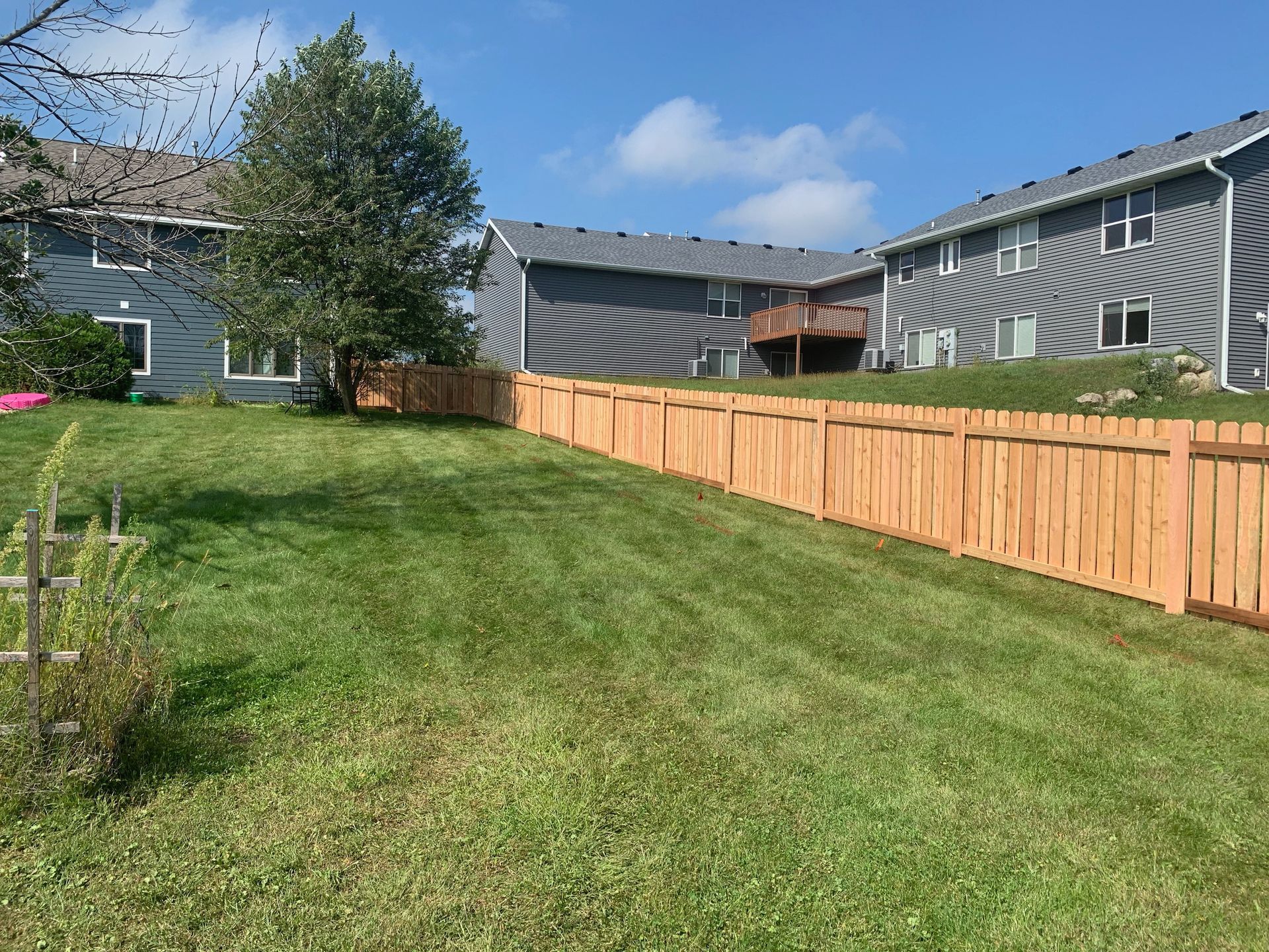 A wooden fence surrounds a lush green yard in front of a house.