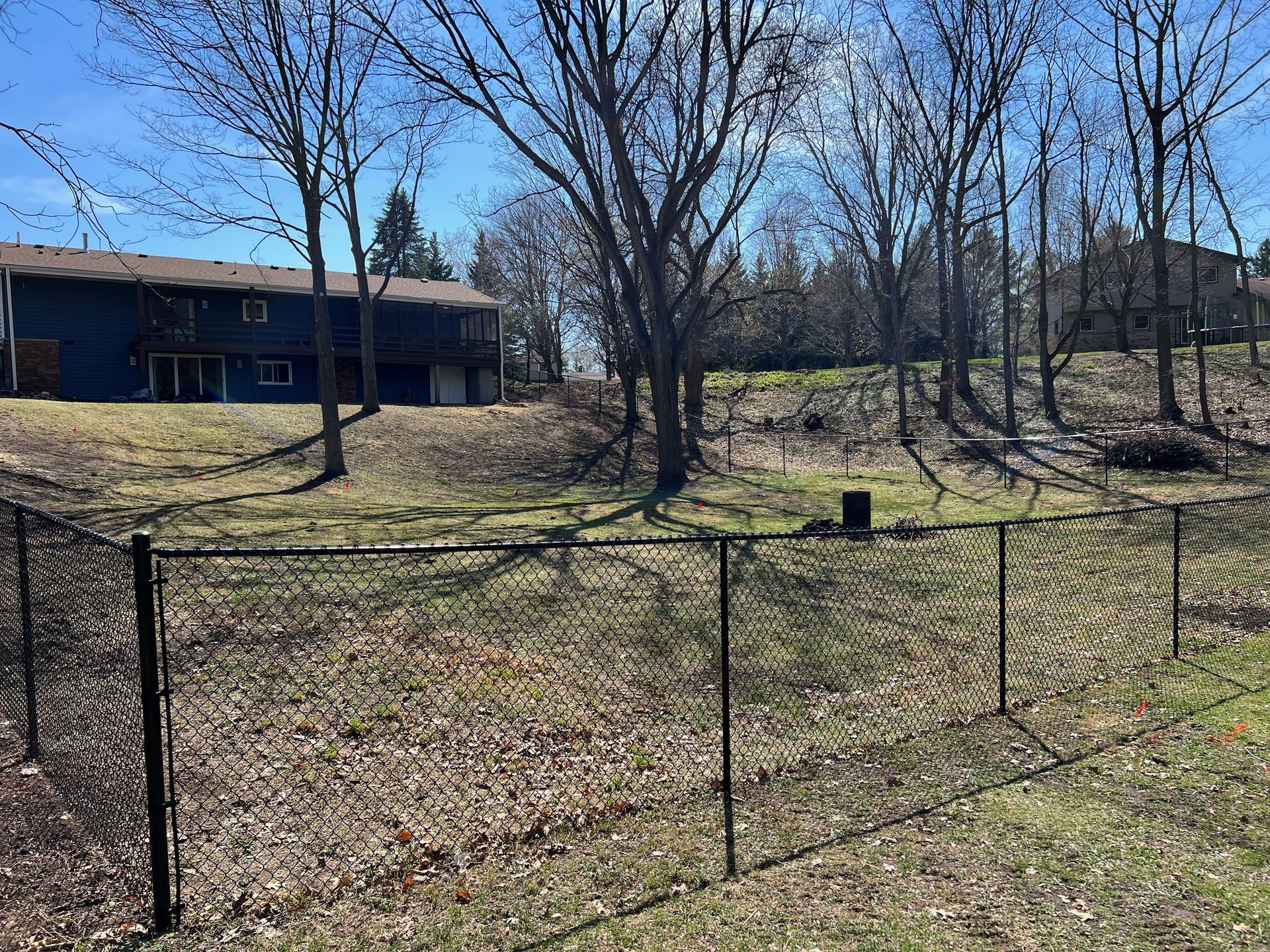 A black chain link fence surrounds a grassy field in front of a house.