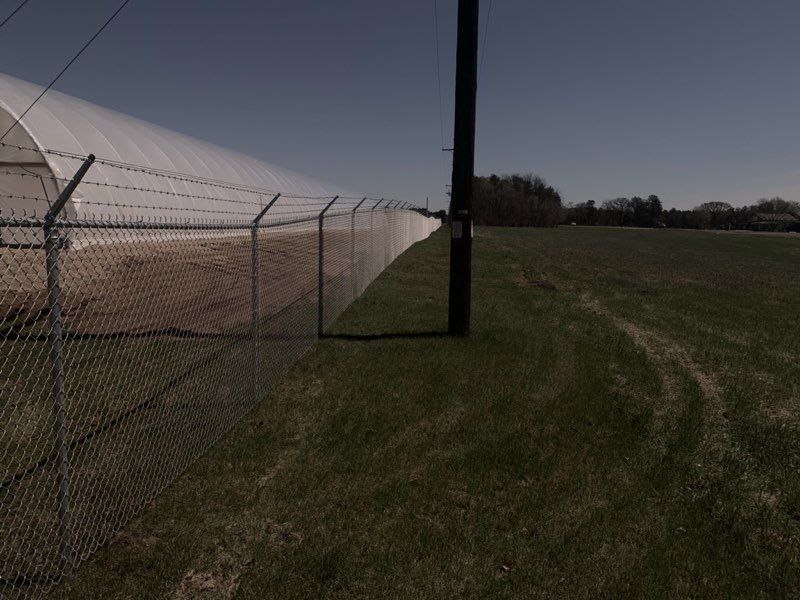 A greenhouse is behind a barbed wire fence