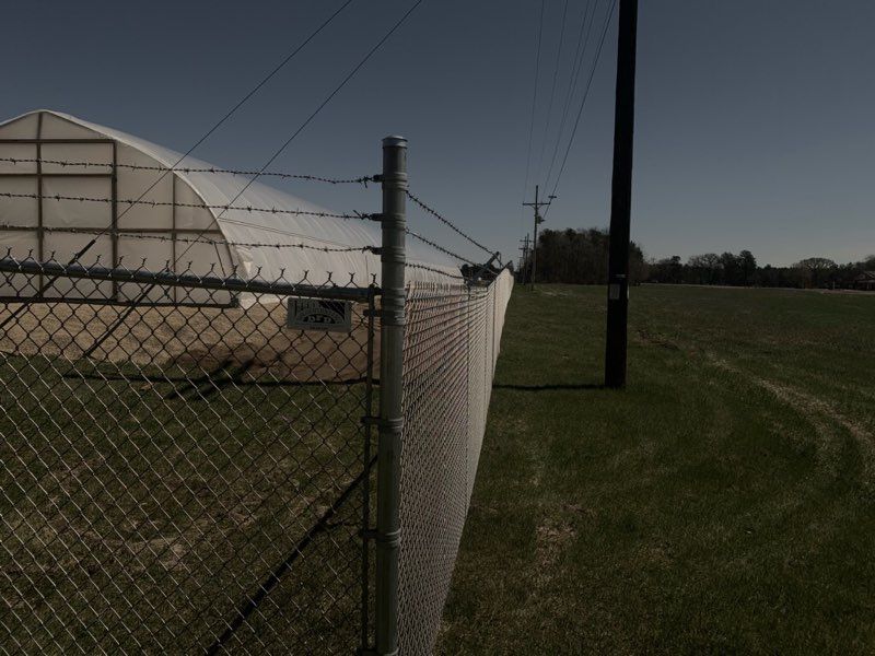 A greenhouse is behind a chain link fence with barbed wire