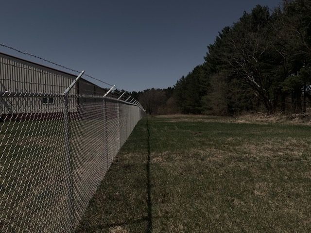 A chain link fence surrounds a field with trees in the background.