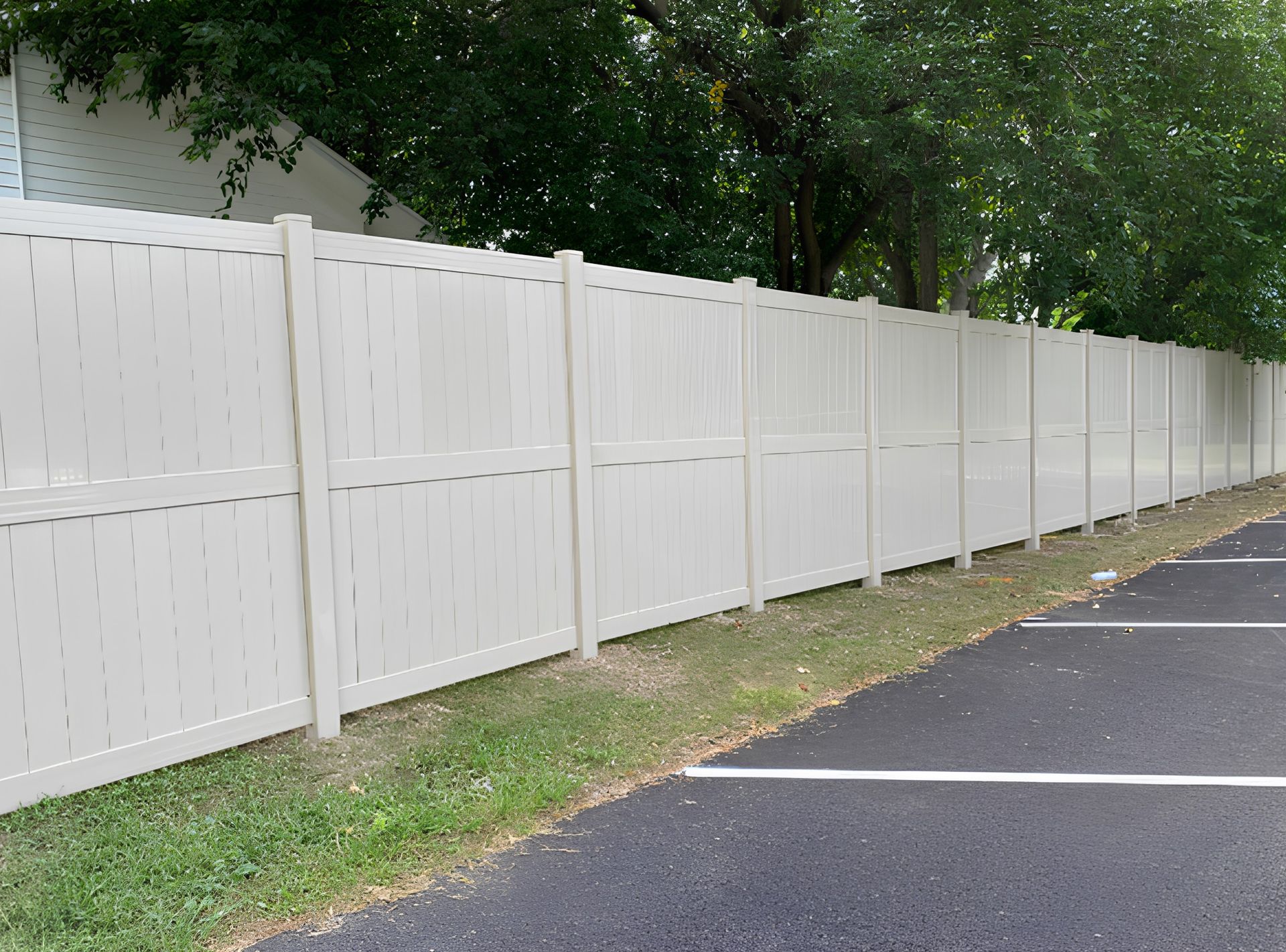 A white fence is along the side of a parking lot