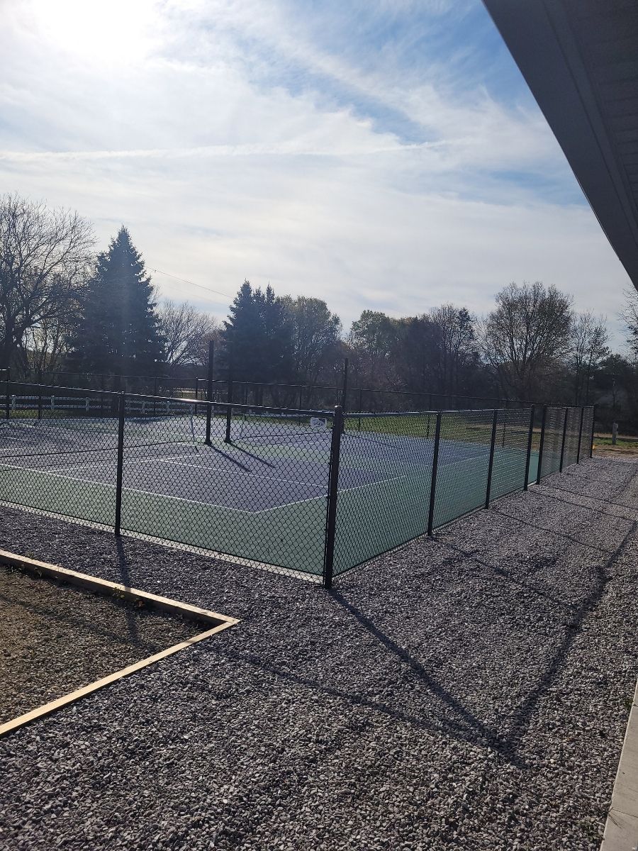 A tennis court behind a chain link fence on a sunny day.