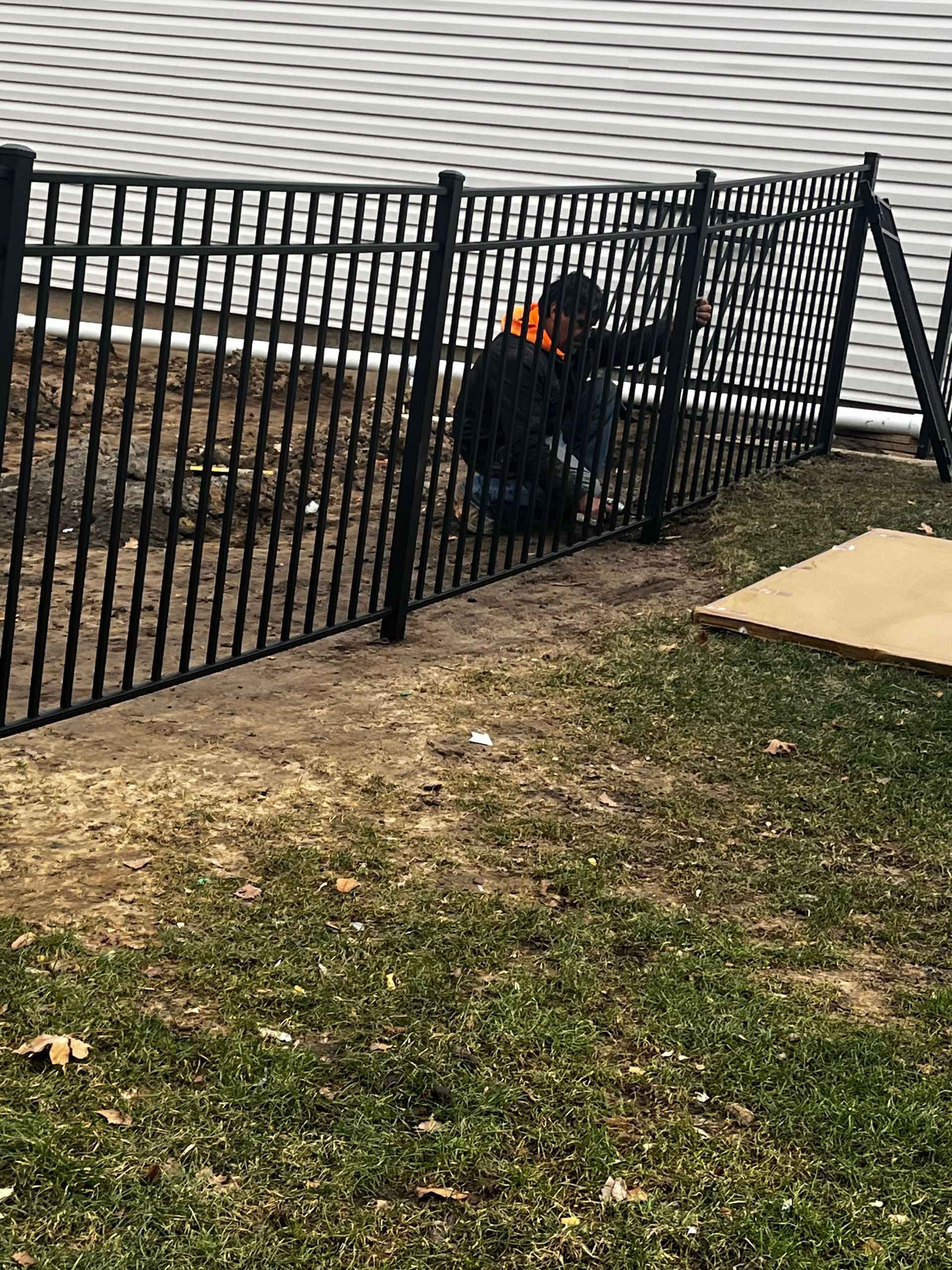 A man is working on a metal fence in a yard.