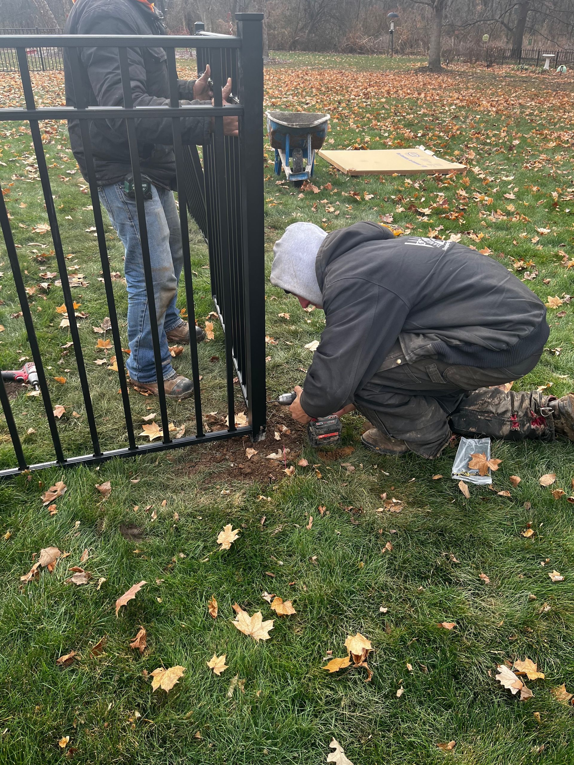 A man is kneeling down in the grass working on a fence.
