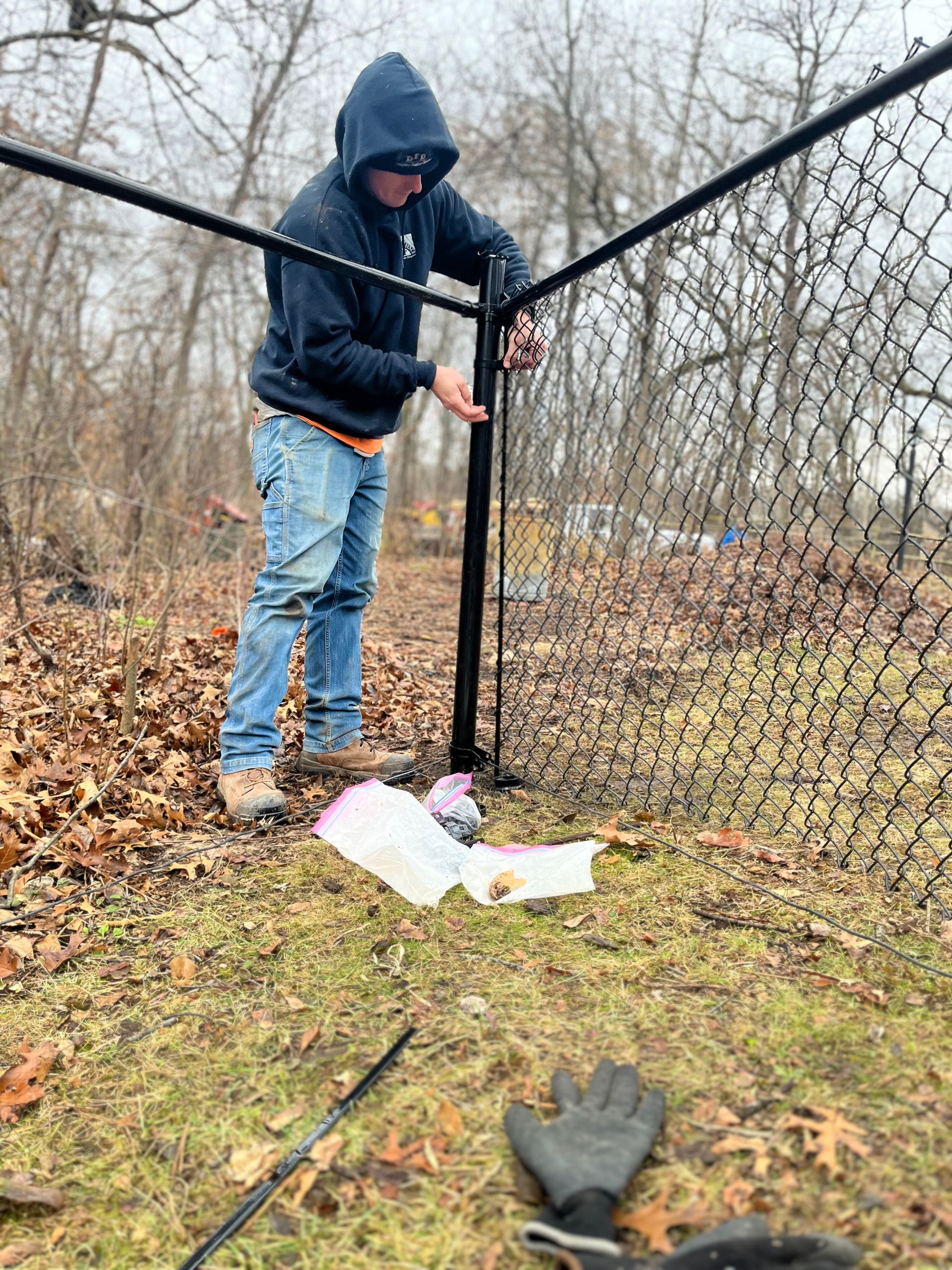 A man in a hoodie is working on a chain link fence.