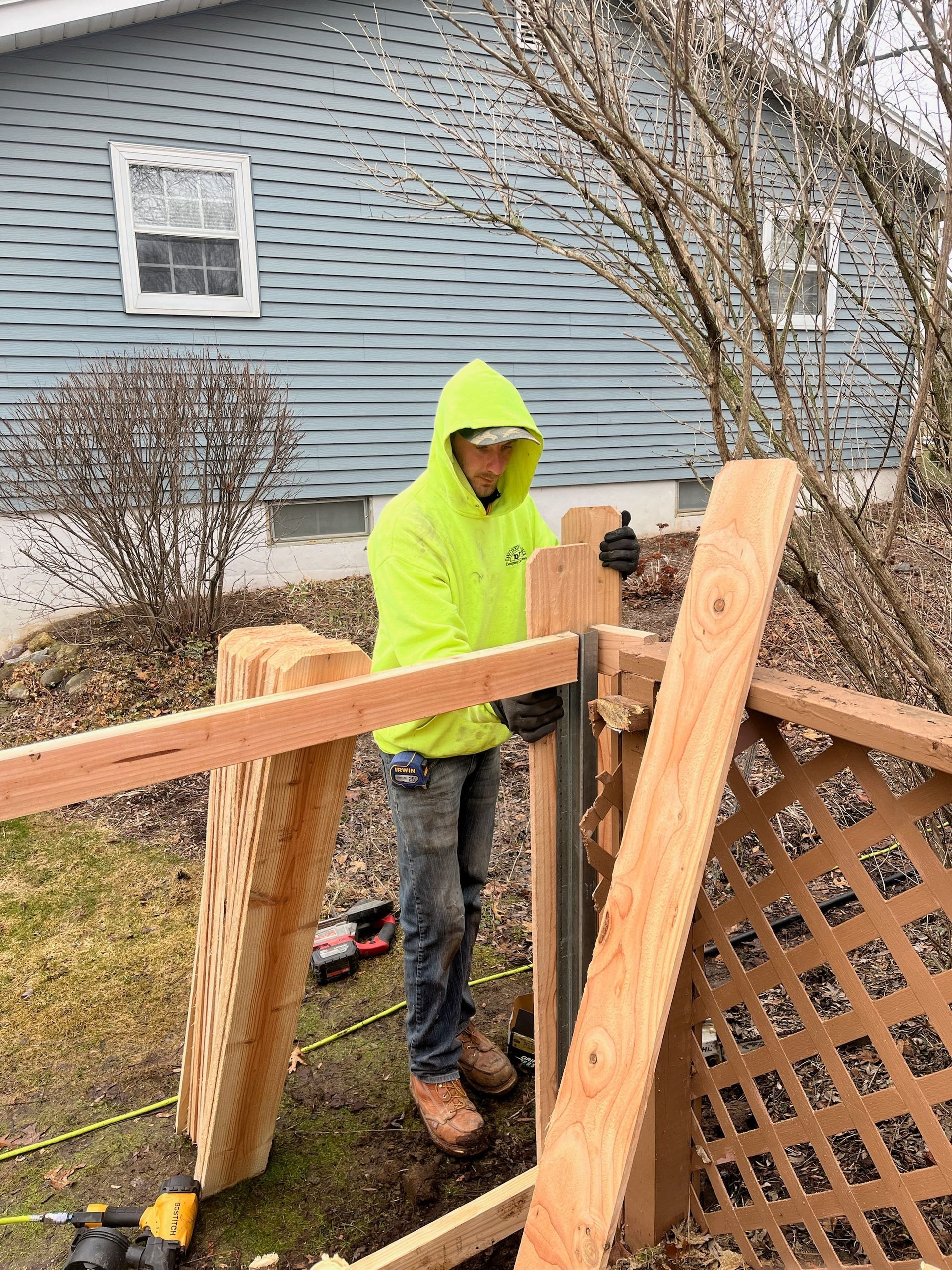 A man is standing next to a wooden fence in front of a house.