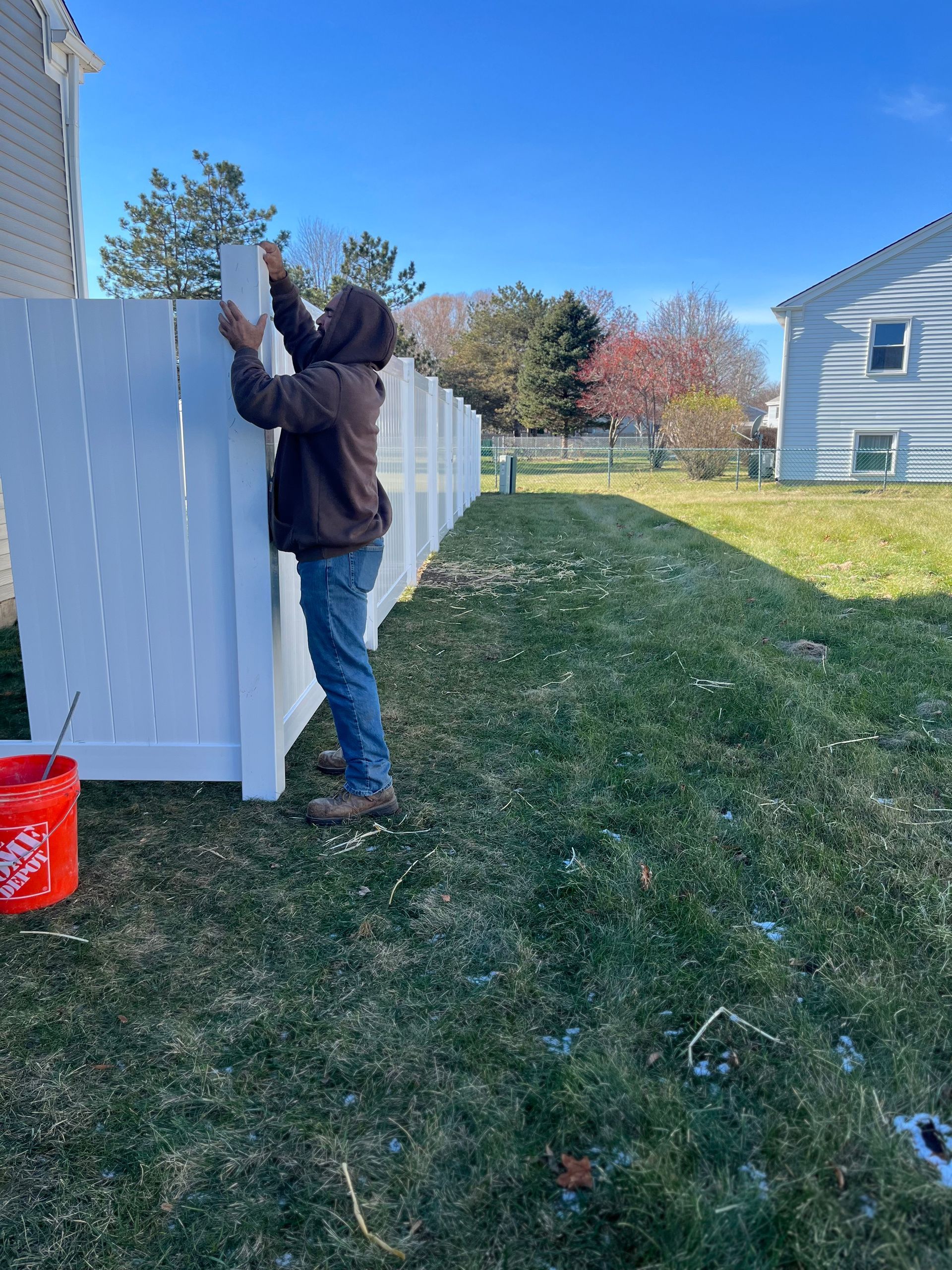 A man is standing next to a white fence in a yard.