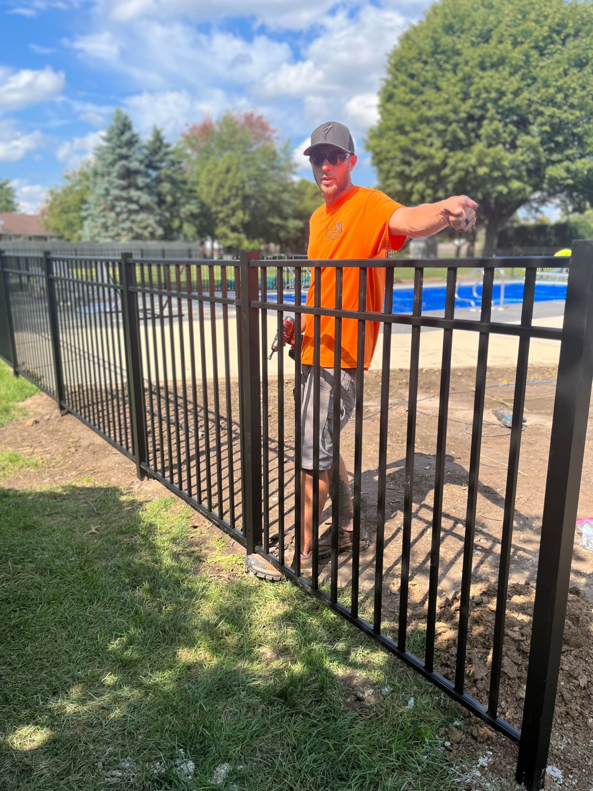 A man in an orange shirt is standing next to a black fence.