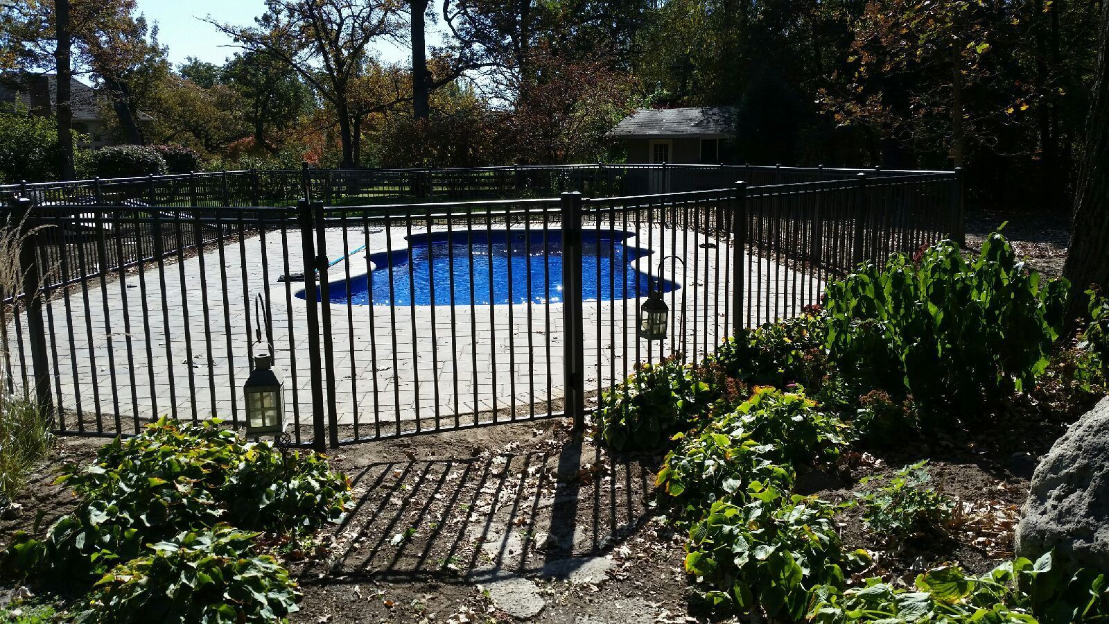 A fence surrounds a large swimming pool in a backyard.