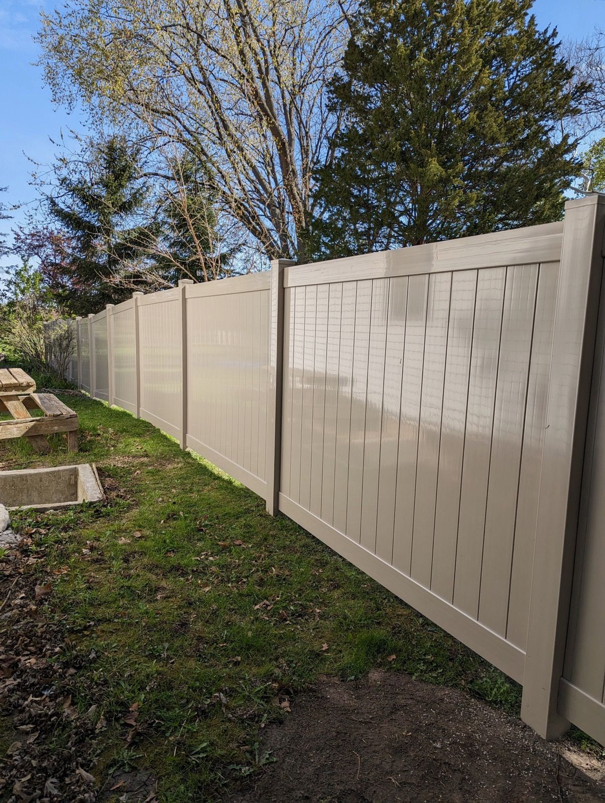 A white fence with holes in it is surrounded by grass and trees.