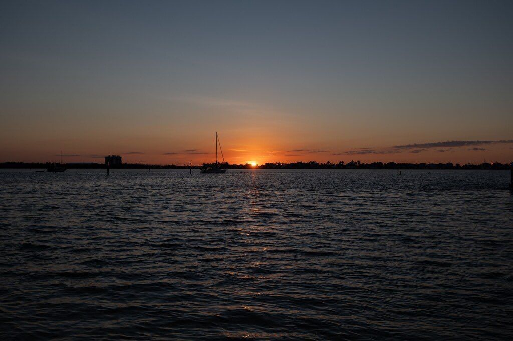 Sunset over a body of water, a sailboat silhouette, and a fiery orange sun.