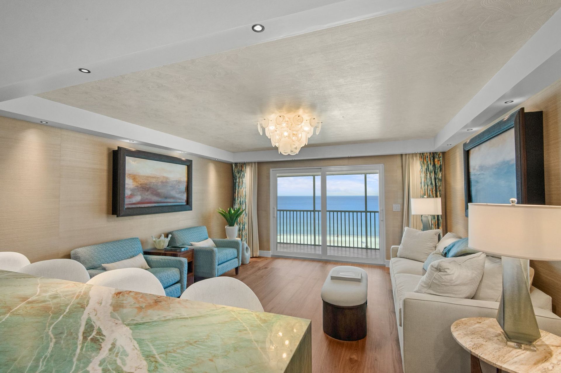 Living room with ocean view, light blue furniture, glass-topped table, and chandelier.