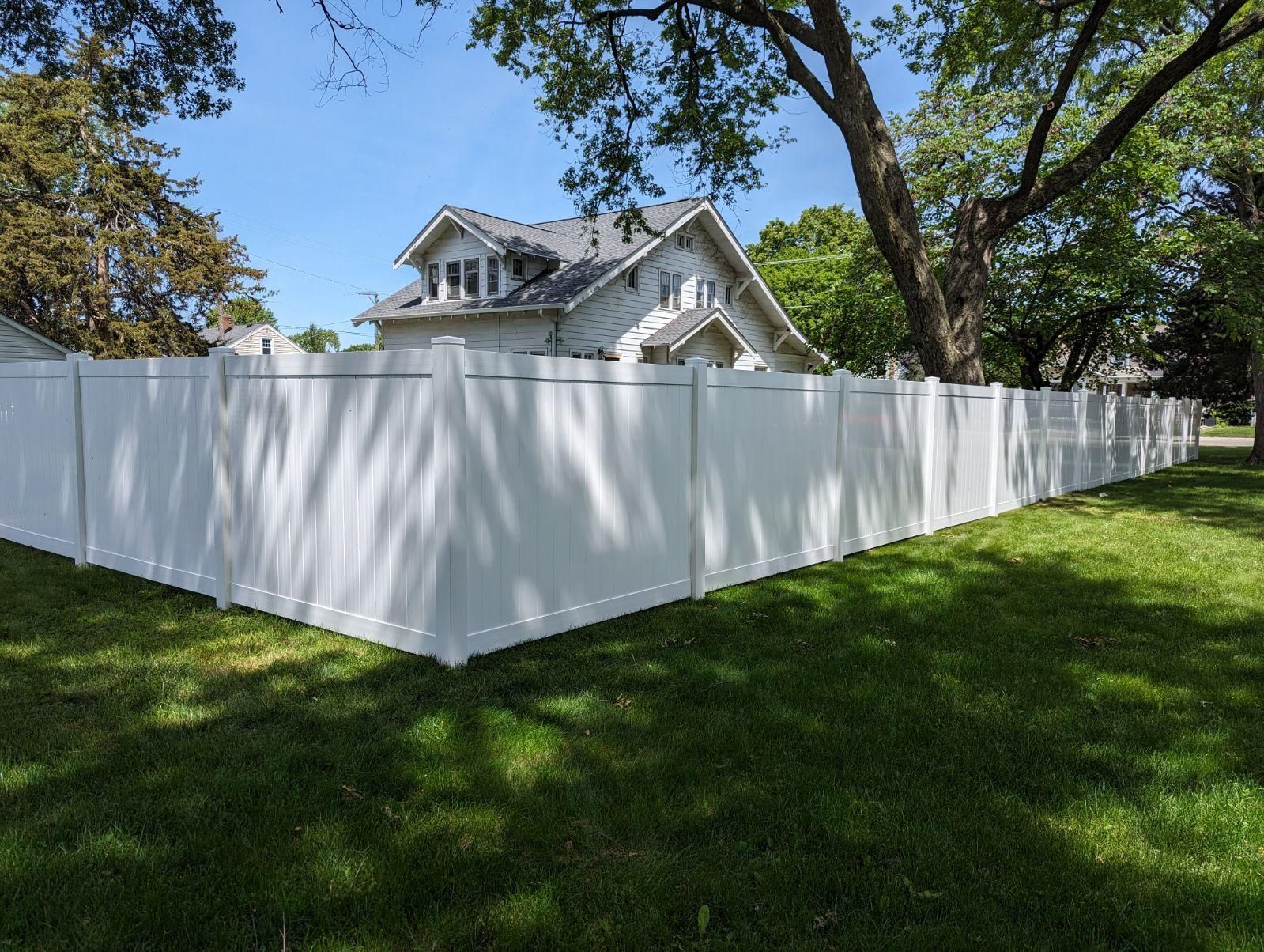 A white fence surrounds a lush green yard in front of a house.