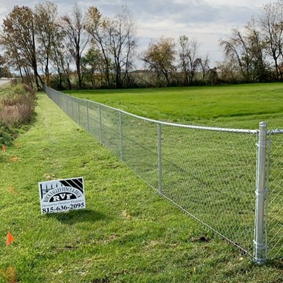 A chain link fence is surrounding a lush green field.