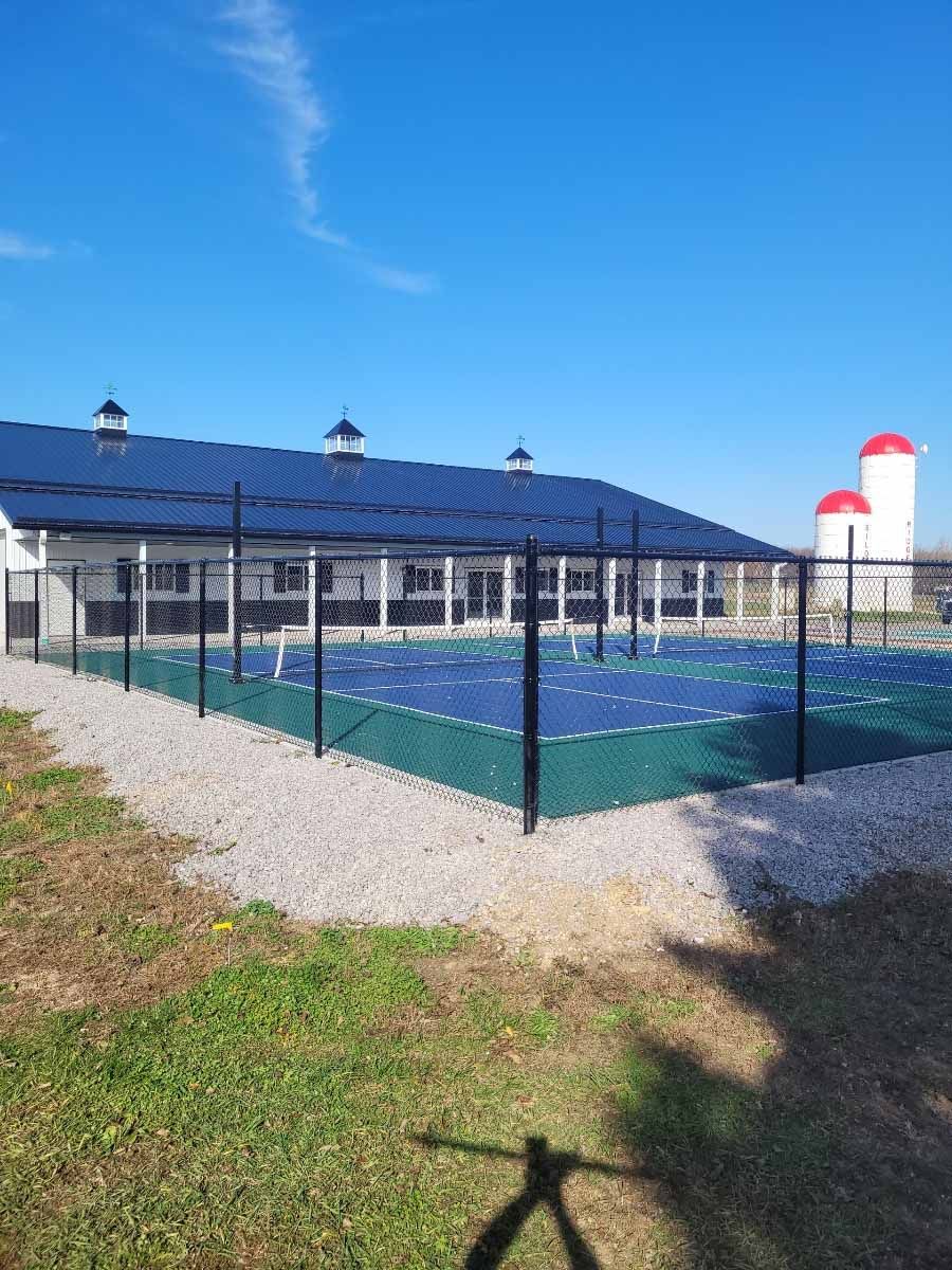 A tennis court with a fence around it and a building in the background.
